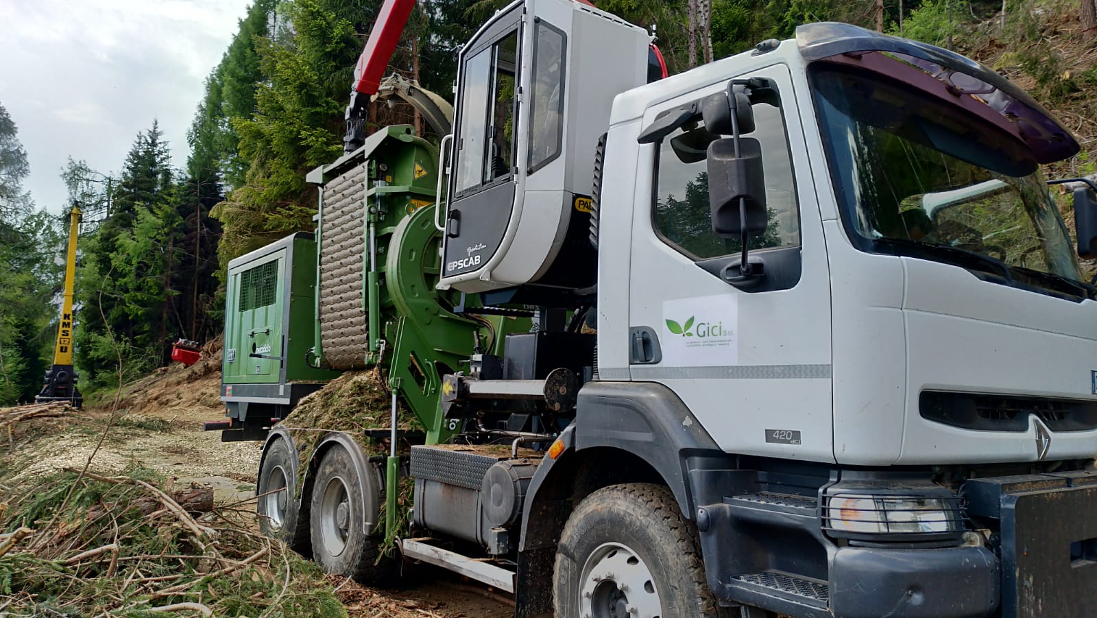 White truck with green timber processing machine in a forest clearing with felled branches nearby.
