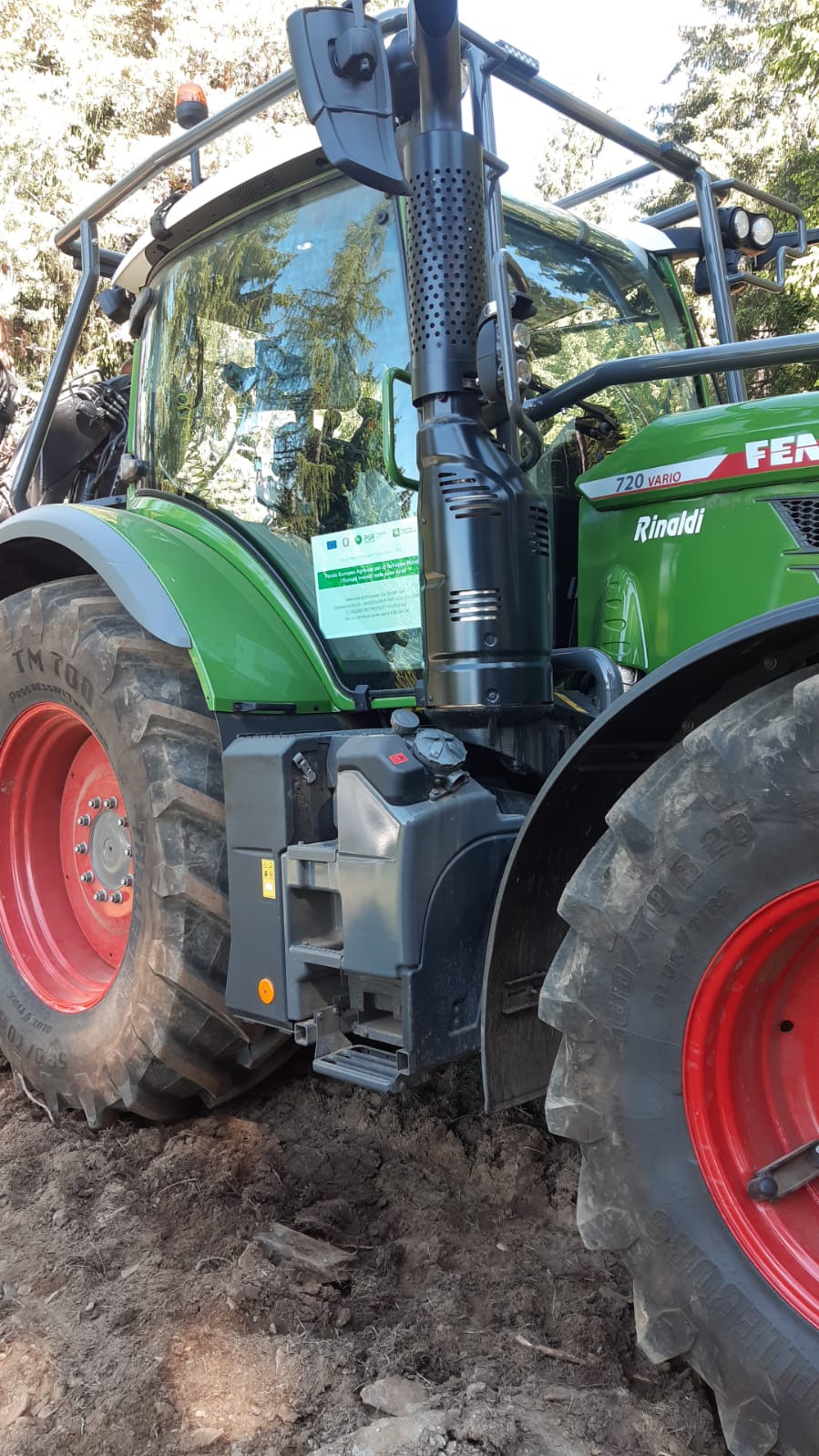 Green Fendt 720 Vario tractor with large red-rimmed tires on dirt ground in a forested area.