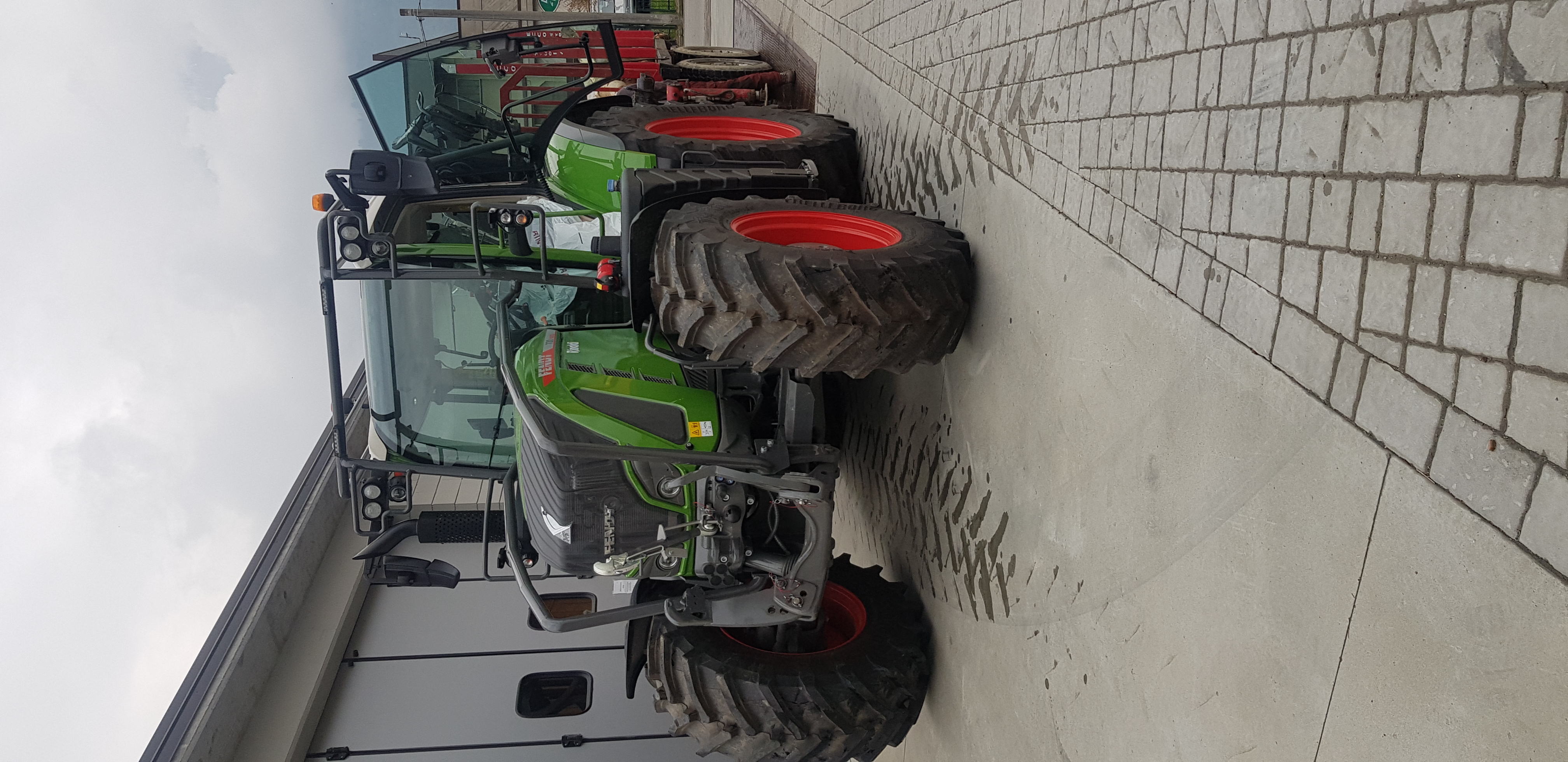 Green Fendt tractor with orange wheels parked on paved surface near building under cloudy sky.