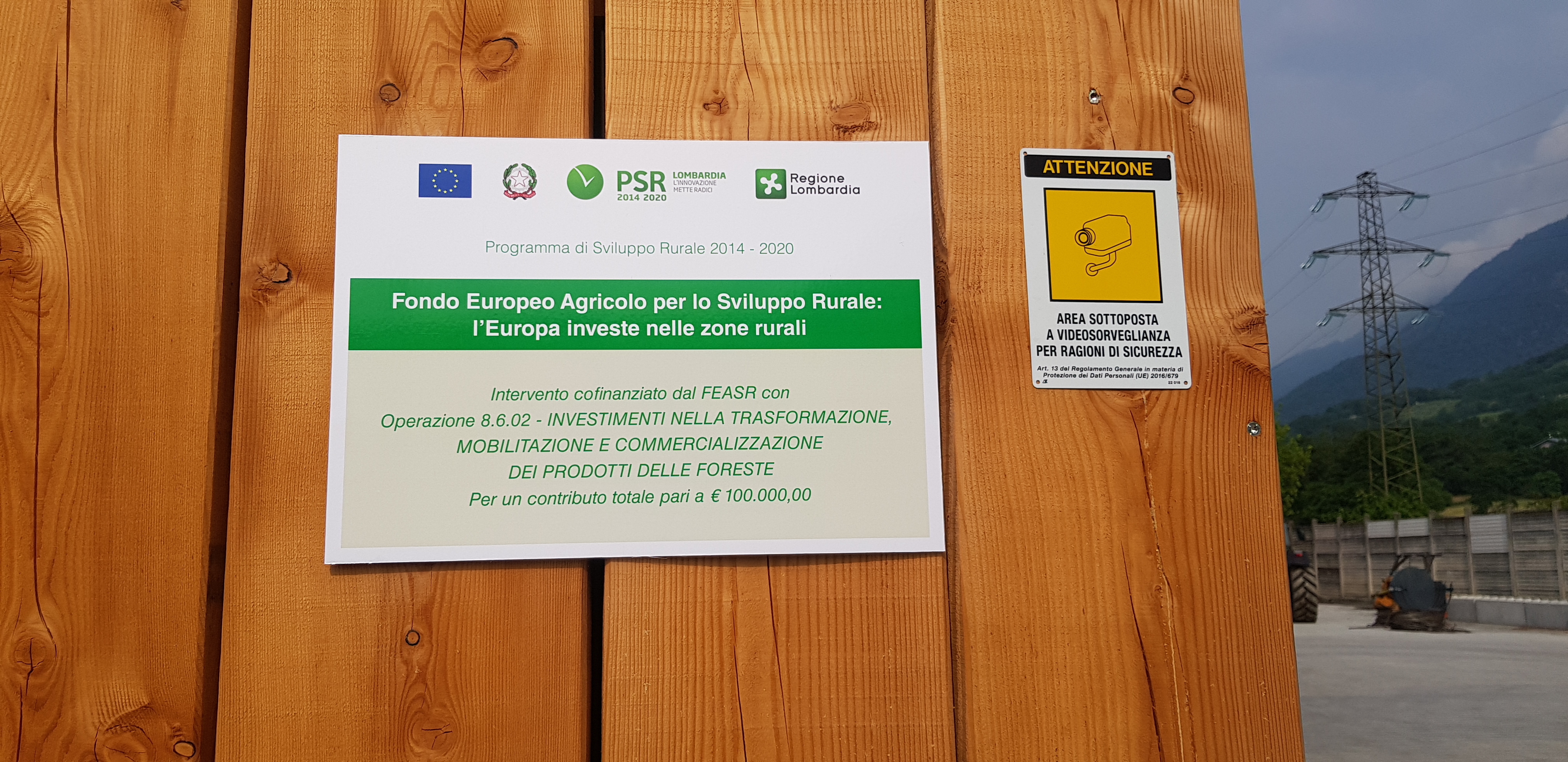 Two signs on wood: EU rural funding program and a CCTV surveillance warning in Italian.