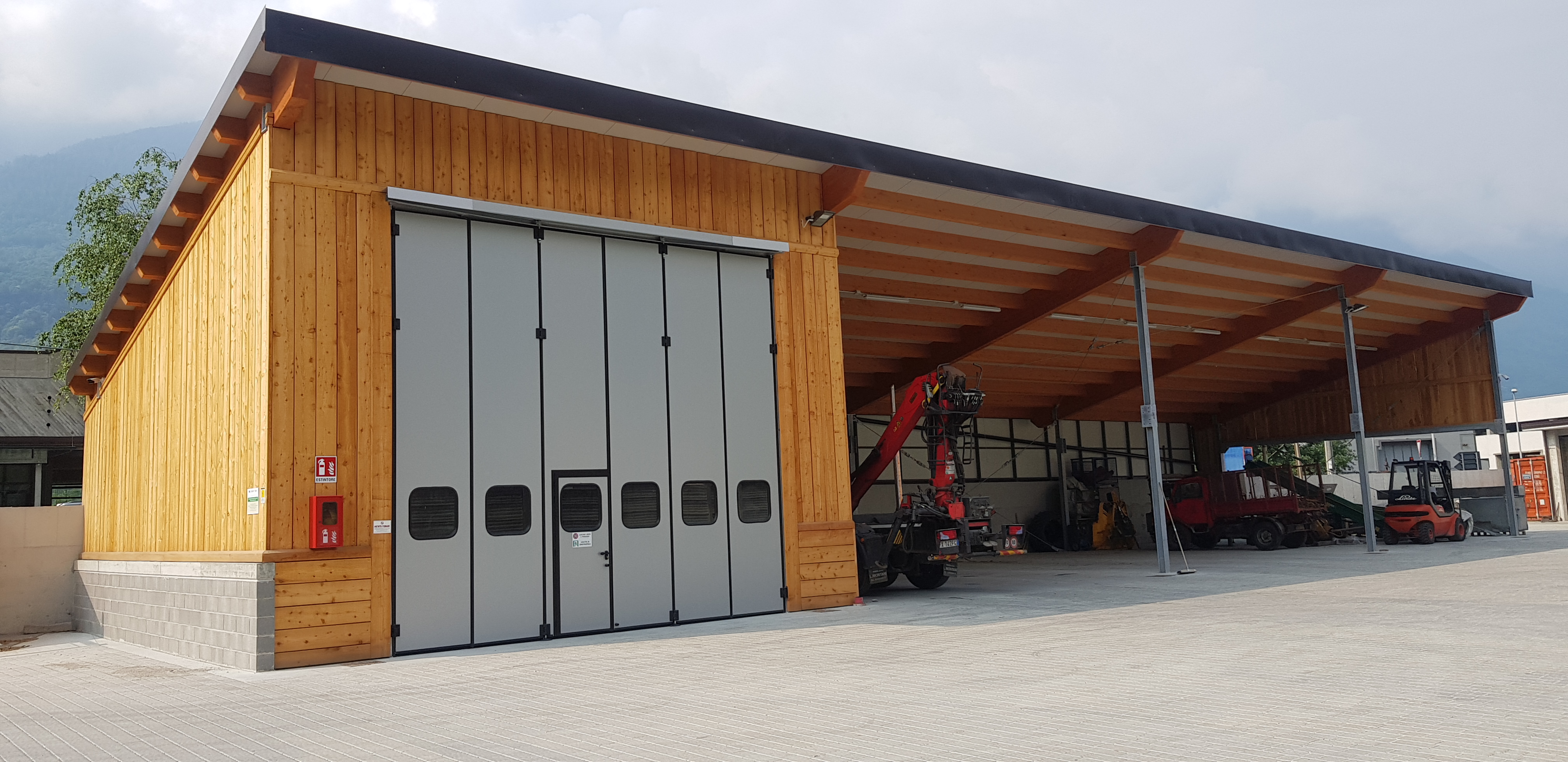 Wooden warehouse with a large closed gray door and open area with parked forklifts and machinery.