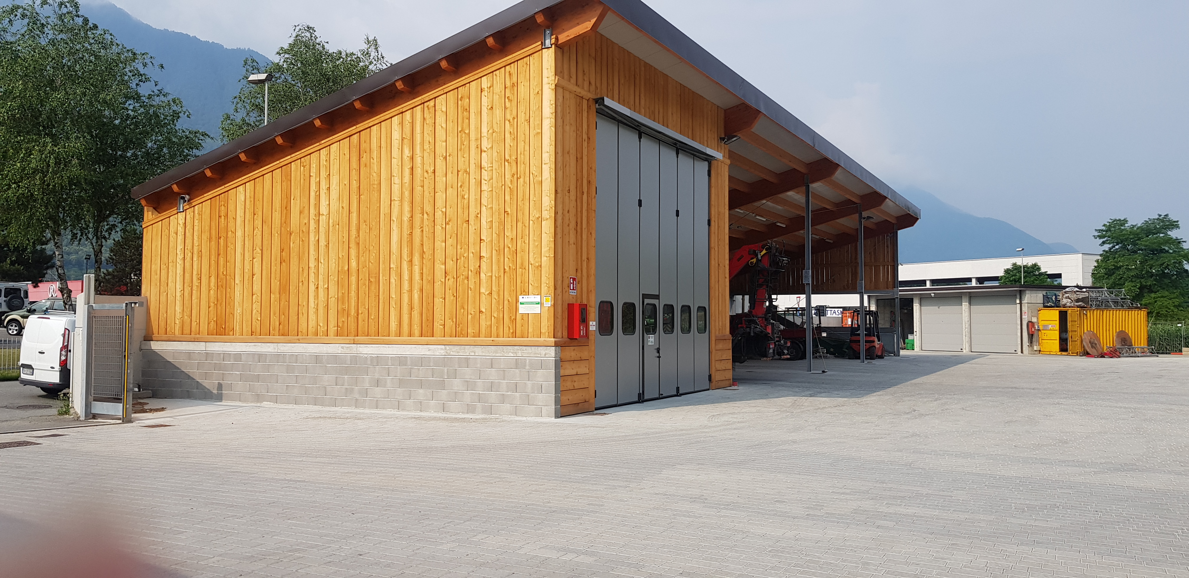 Wood and concrete industrial building with large metal doors and equipment inside, mountains in background.