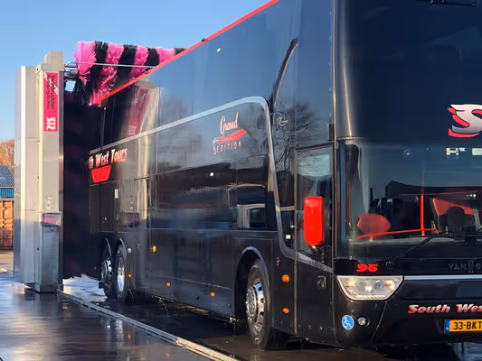 Een zwarte tourbus wordt gewassen met een automatische wasinstallatie met roze borstels.