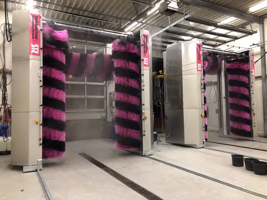 Automatische wasstraat voor voertuigen met verticale en horizontale roterende borstels in roze en zwart.