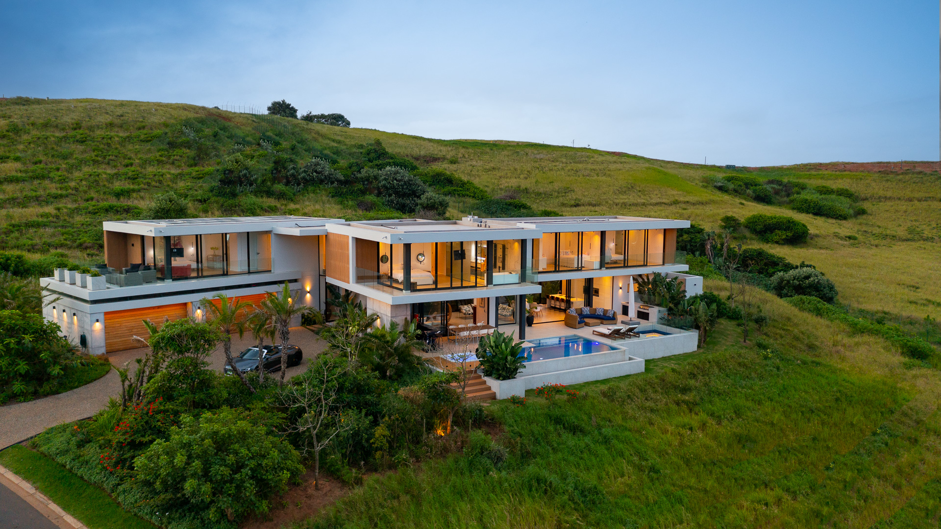 Aerial rear elevation of House Django, a bespoke contemporary residence designed by Gerhard Architect in Zululami Luxury Coastal Estate on KwaZulu-Natal's North Coast. The image showcases the home's cantilevered rooflines, expansive floor-to-ceiling glazing, wraparound terraces, infinity pool, outdoor entertainment spaces and landscaped gardens, demonstrating how the architecture is carefully positioned to maximise privacy, natural light and uninterrupted views across the estate's protected coastal greenbelt.