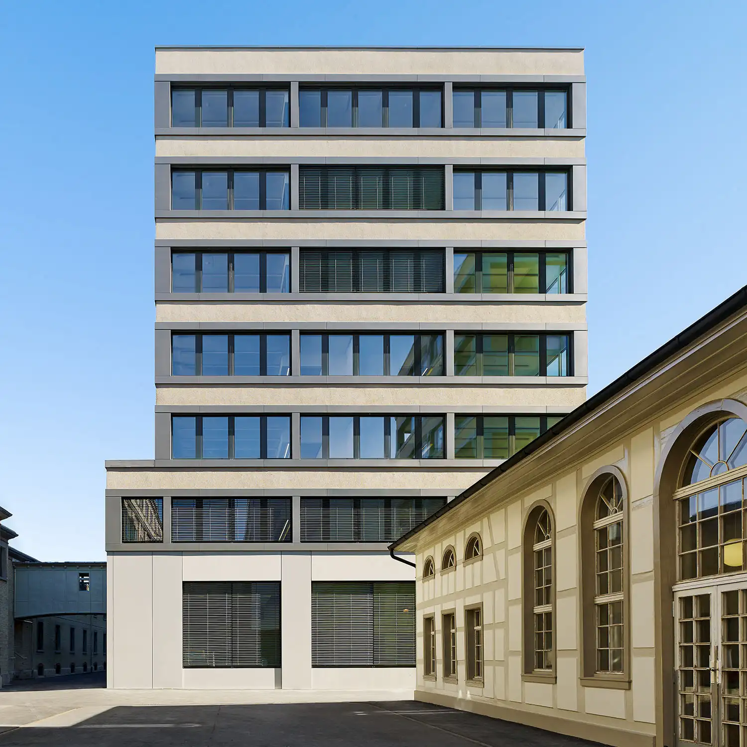 Zeitgenössisches Bürogebäude mit klar gegliederter Aluminiumfassade neben historischem Bauwerk, verbindet moderne Architektur mit hochwertiger Beschichtungsqualität.