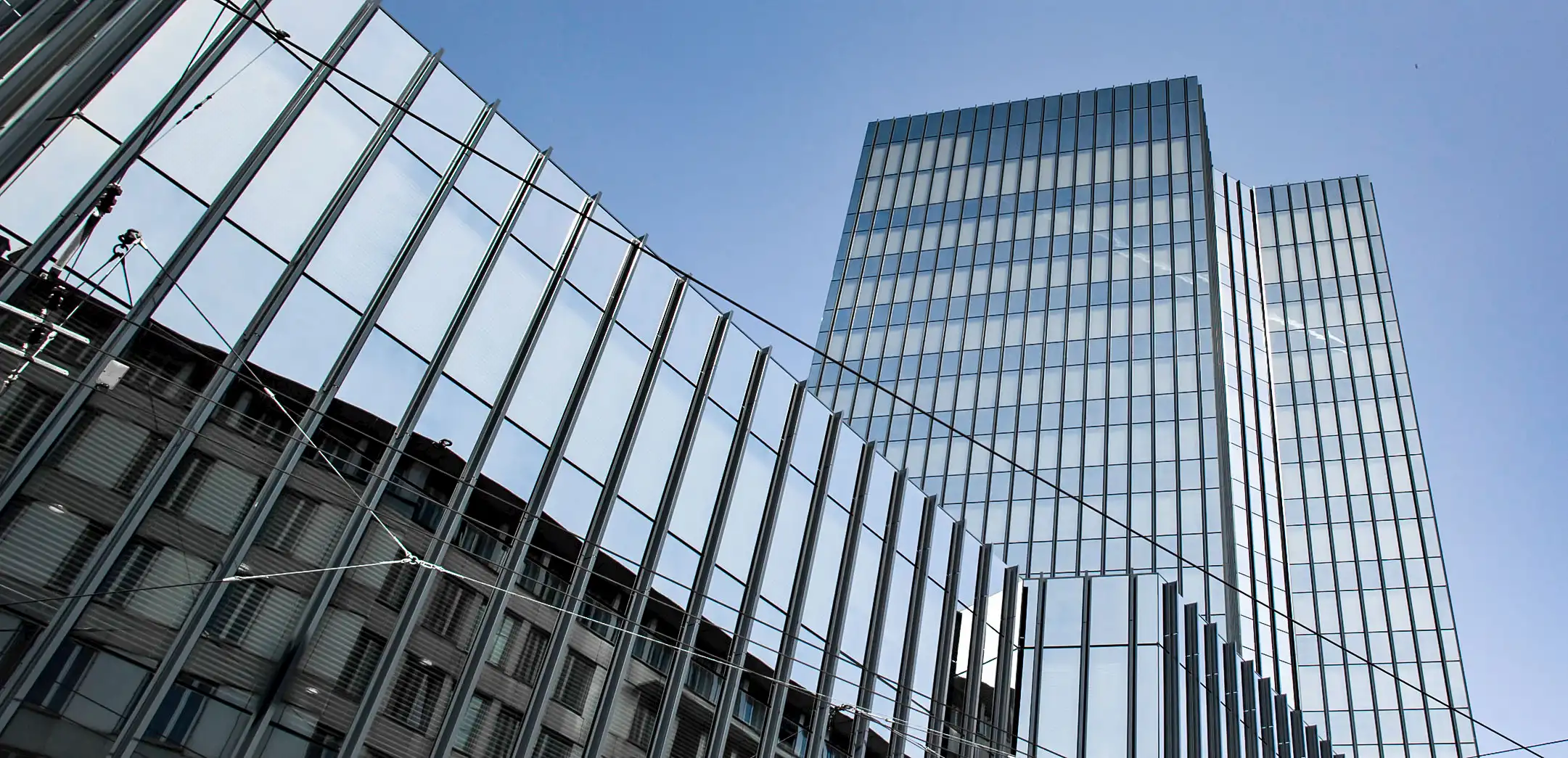 Moderne Glasfassade mit spiegelnder Aluminiumbeschichtung vor blauem Himmel, Sinnbild für hochwertige Architektur und langlebige QUALICOAT Oberflächen.