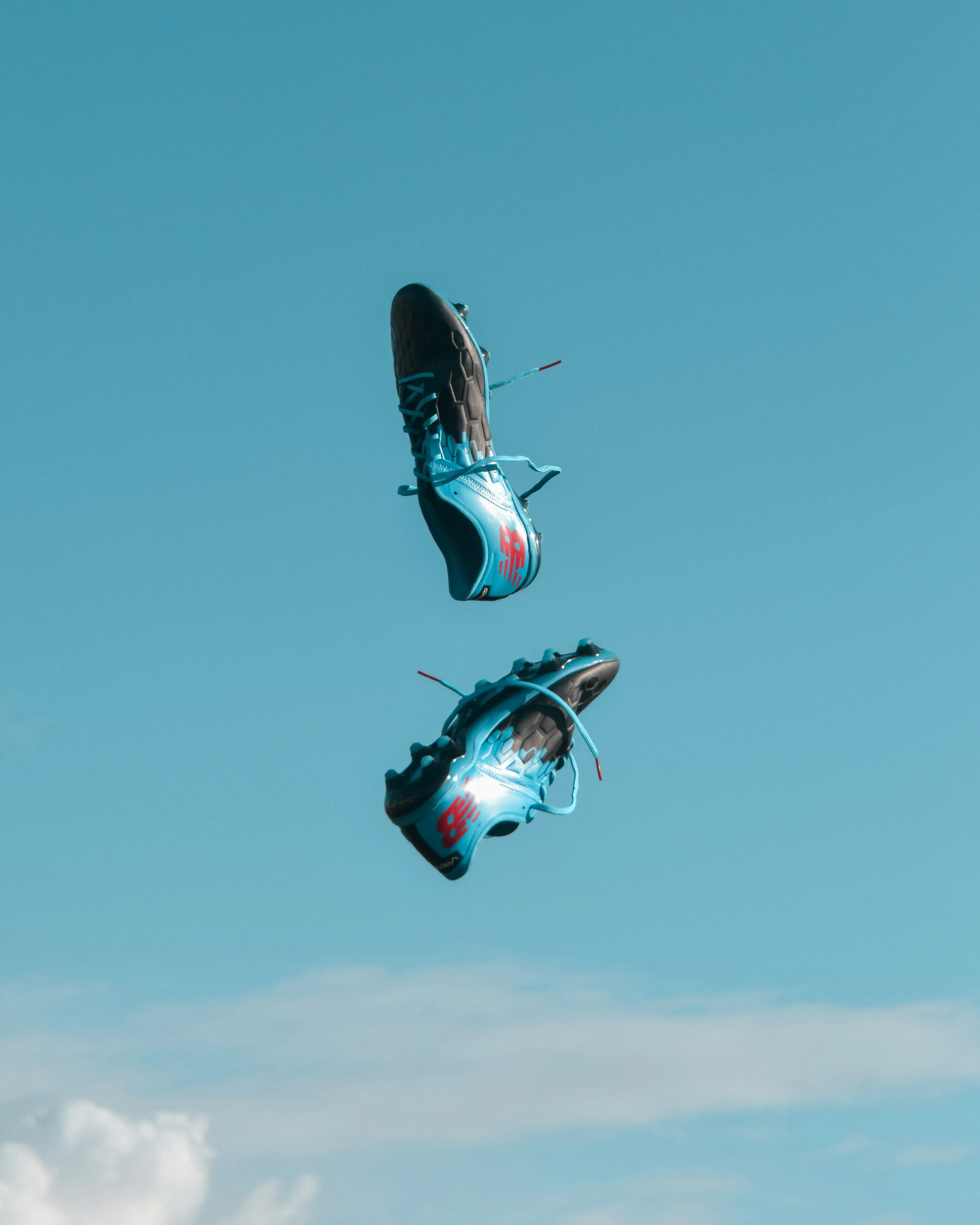 Pair of black and blue soccer cleats with red logos suspended in a clear blue sky.
