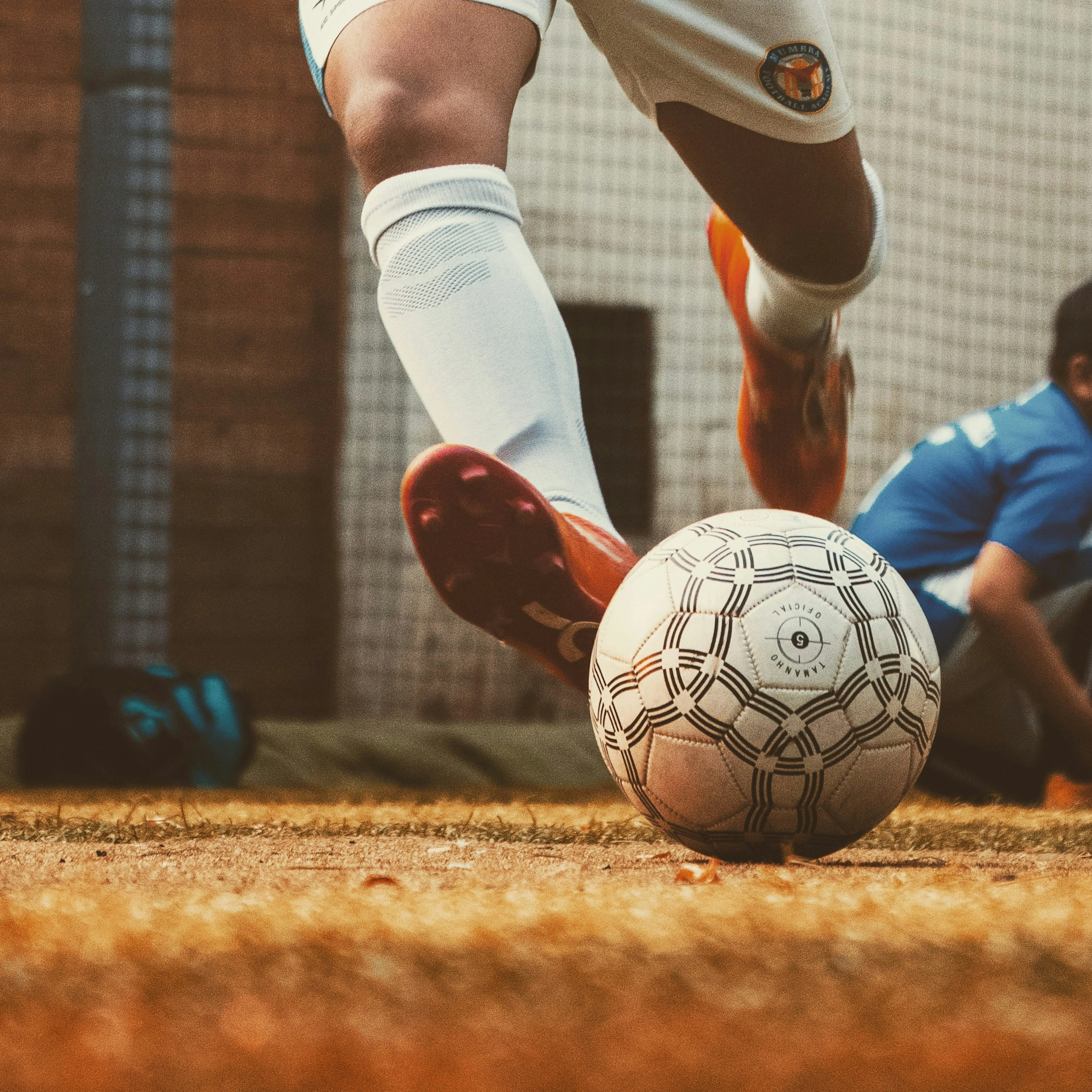 Close-up of a soccer player in white kicking a patterned ball on a grass field near a goal net.