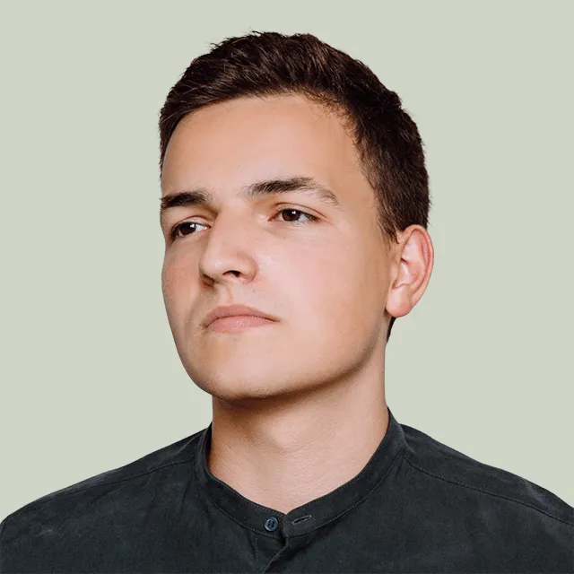 Young man with short dark hair wearing a dark shirt looking away on a light gray background.