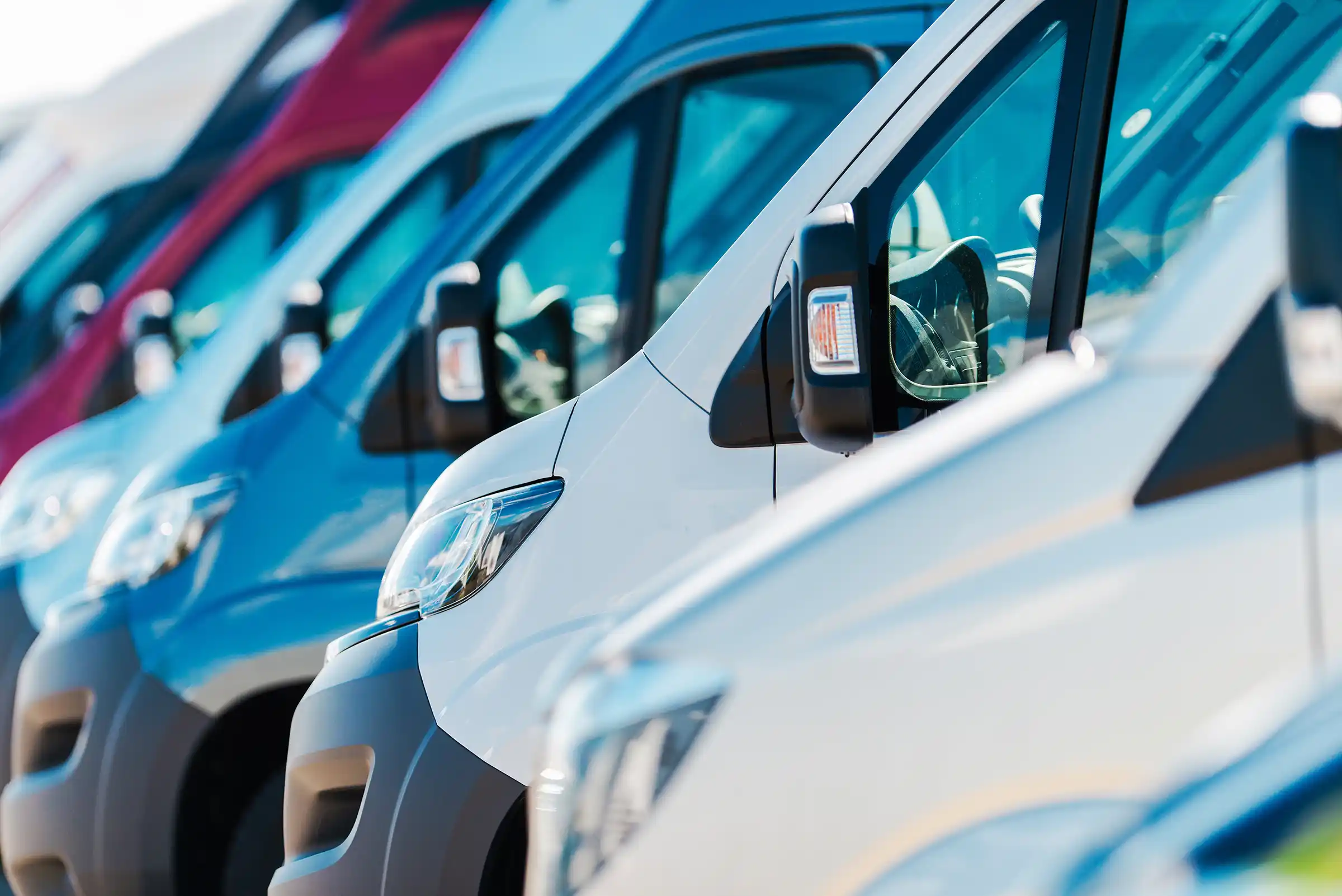 Close-up of a row of white and blue cargo vans parked diagonally outdoors.