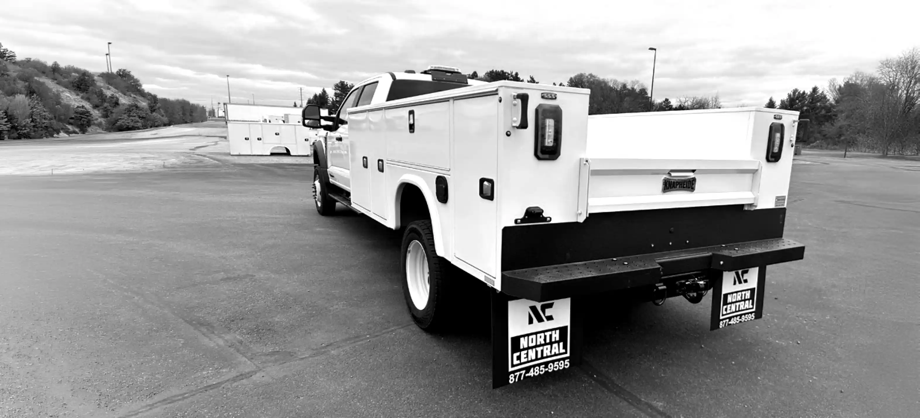 White utility service truck with storage compartments and North Central mud flaps on a paved lot.