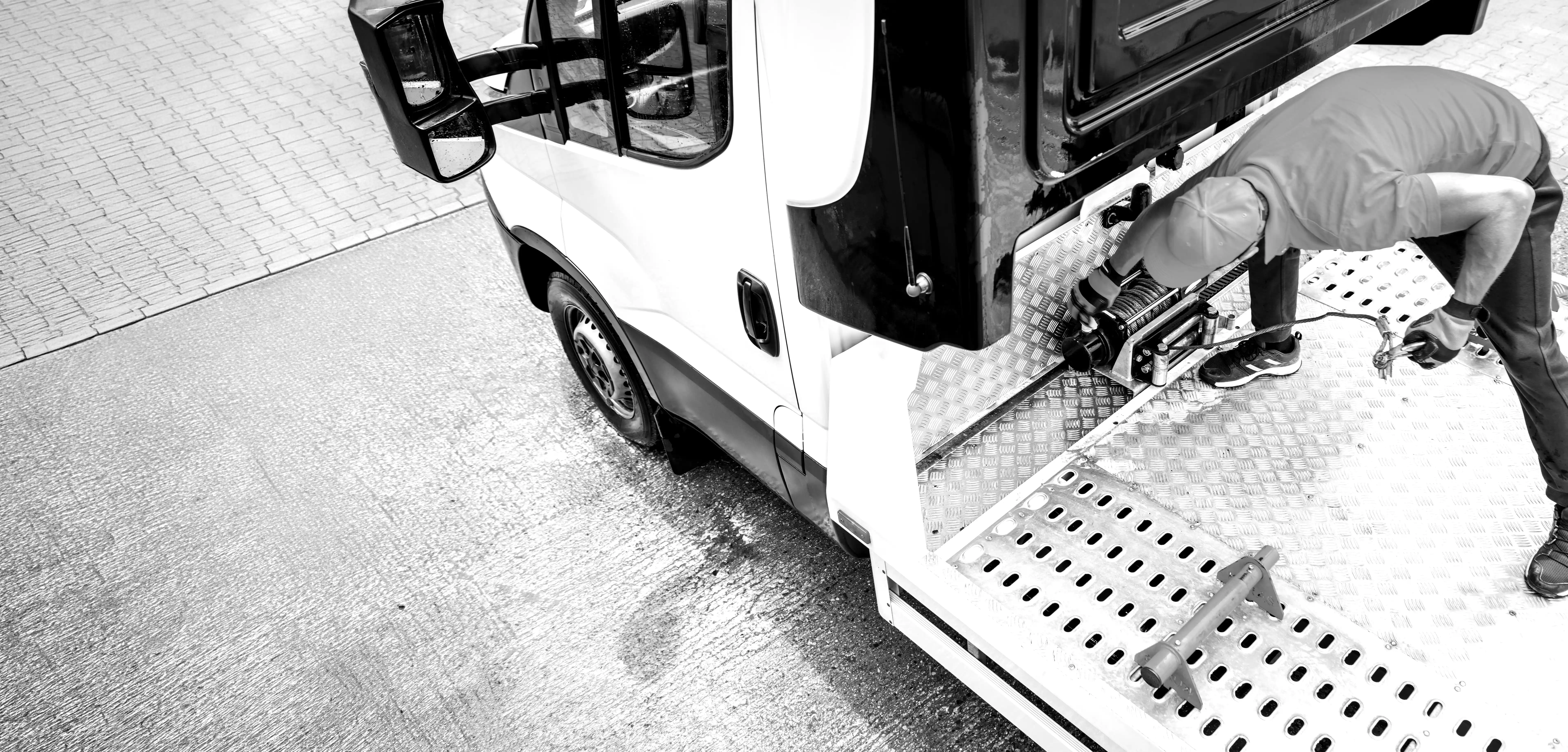 Man in cap attaching winch cable inside a vehicle cargo area with perforated metal floor panels.