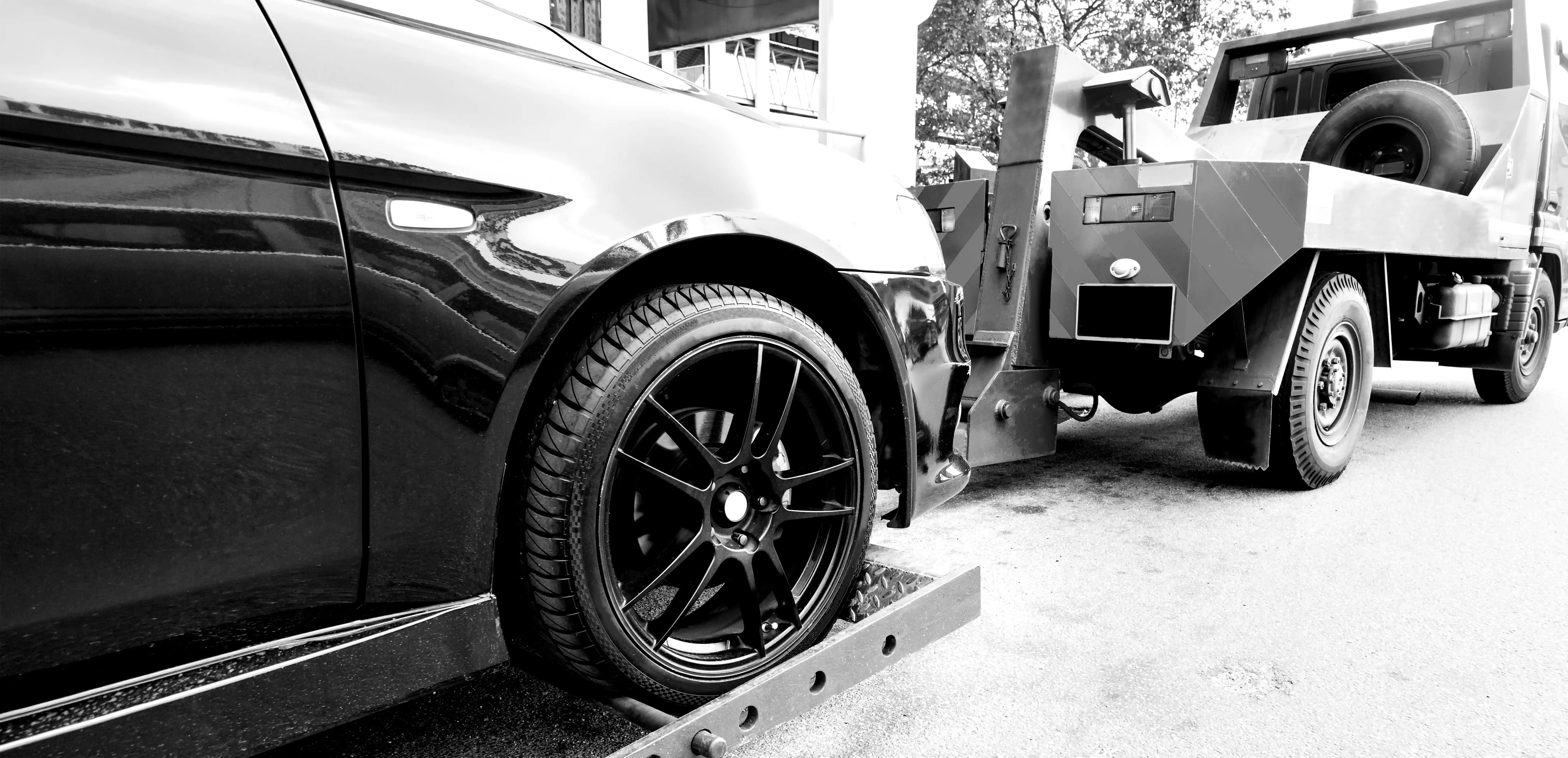 Close-up of a car's front wheel being loaded onto a tow truck's platform on a city street.