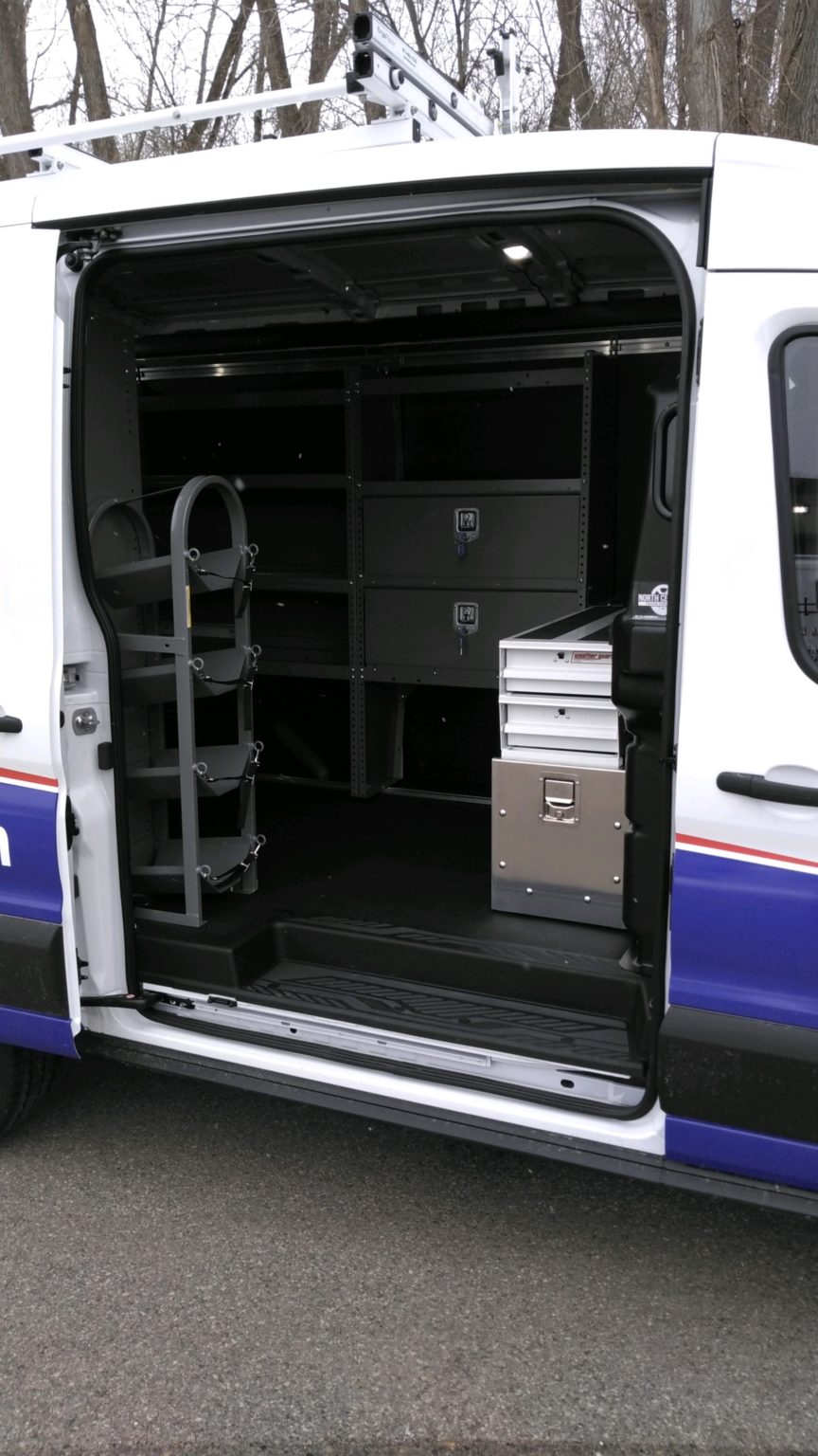 Open side door of white van showing organized black storage shelves and metal toolboxes inside.