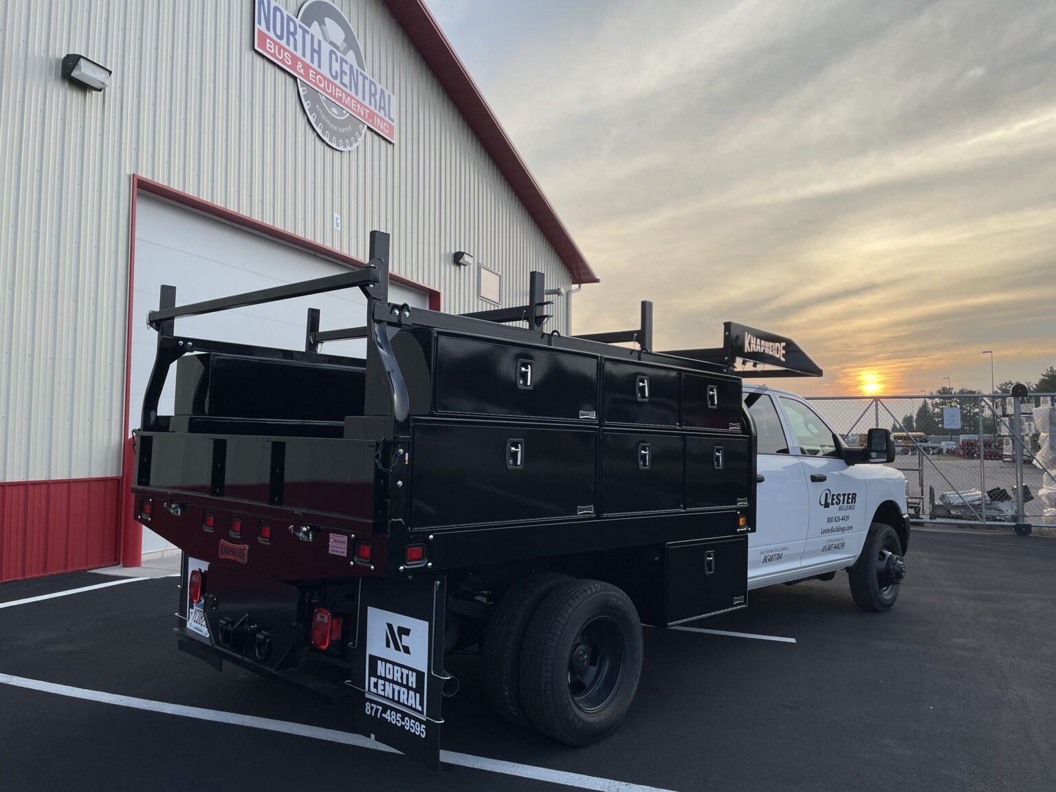 White work truck with black storage compartments parked outside North Central Bus & Equipment building at sunset.