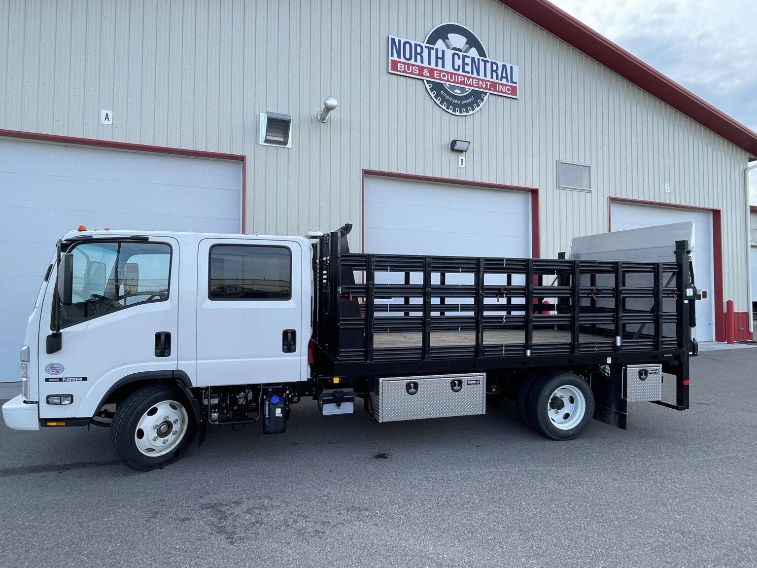 White flatbed truck with black metal side rails parked outside a building with North Central sign.