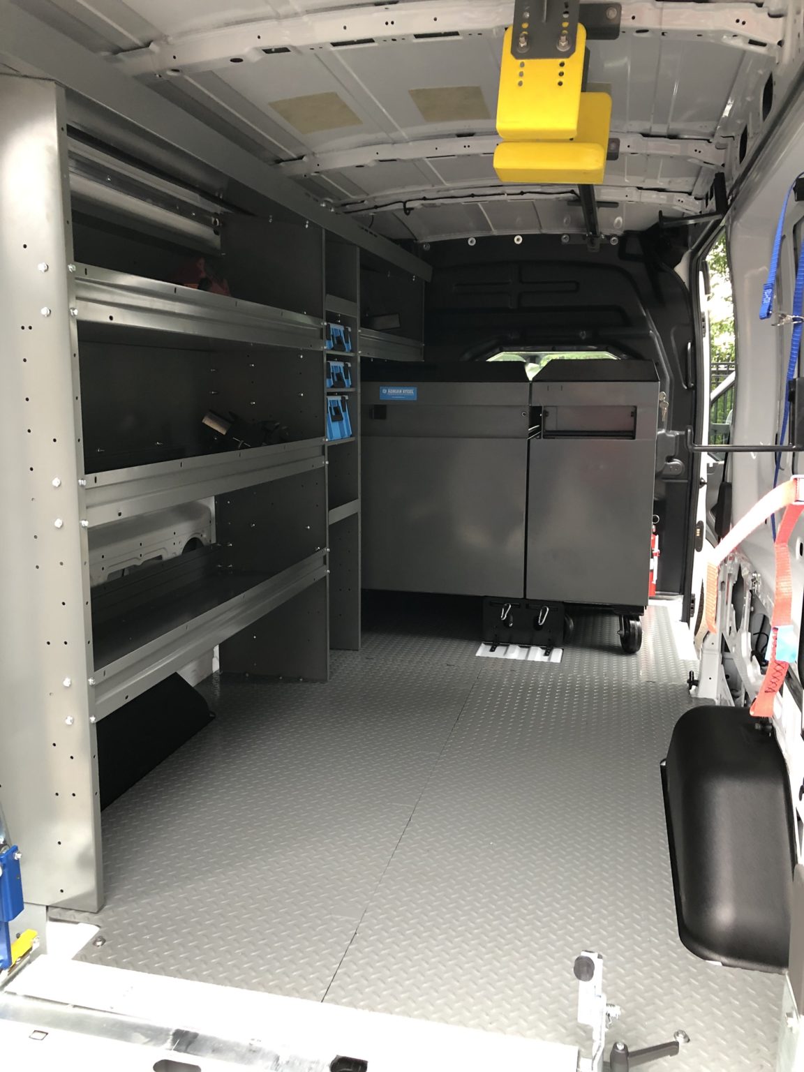 Interior of a work van with metal storage shelves and a large gray tool cabinet on the right.