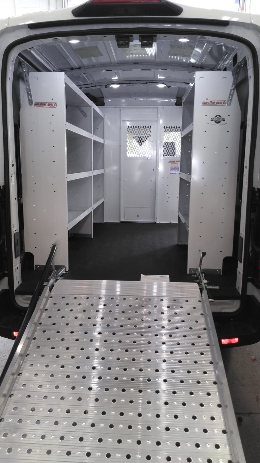Interior of a white work van with metal shelving units and a metal loading ramp extended from the back.