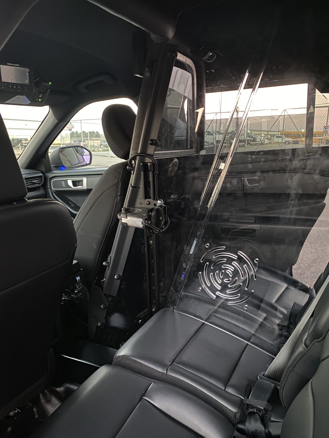 Interior of a vehicle showing black leather seats and a transparent partition with ventilation near the front seats.