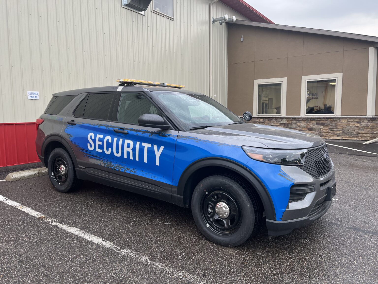 Gray and blue security SUV with yellow roof lights parked outside a building.