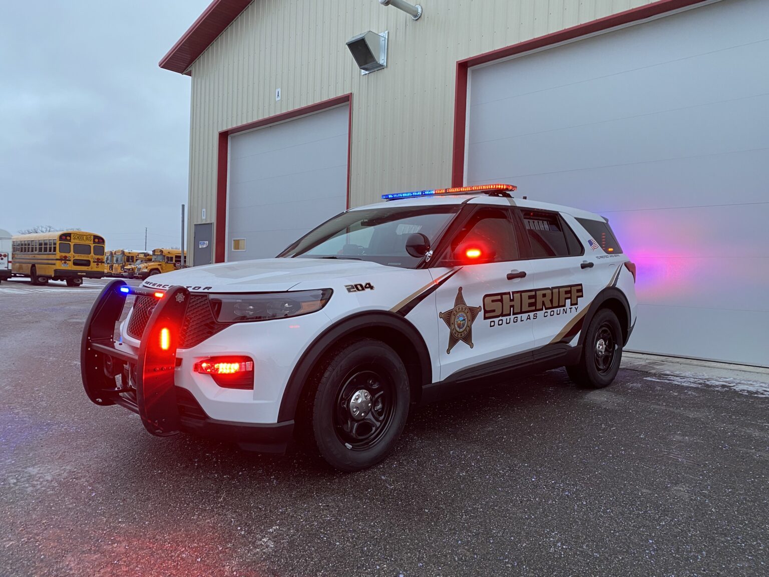 White Douglas County sheriff SUV with flashing red and blue lights parked outside a garage.