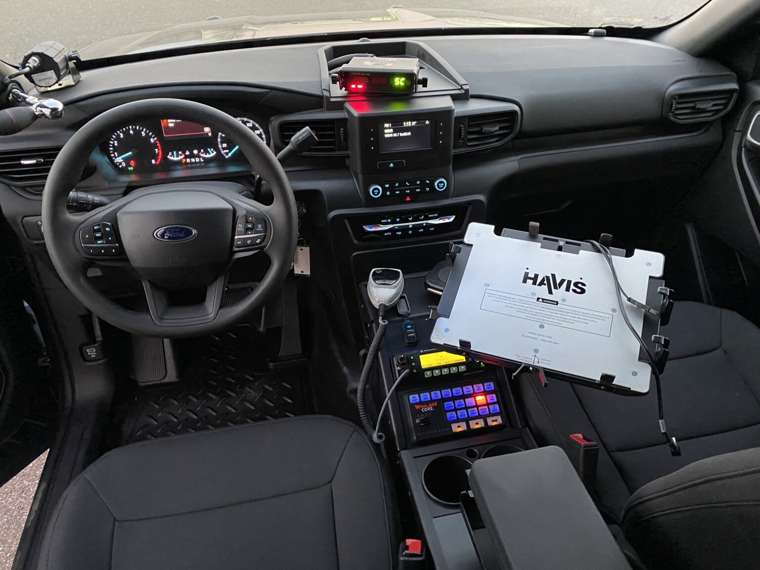 Interior of a Ford vehicle with dashboard, steering wheel, radio, and police equipment on the center console.