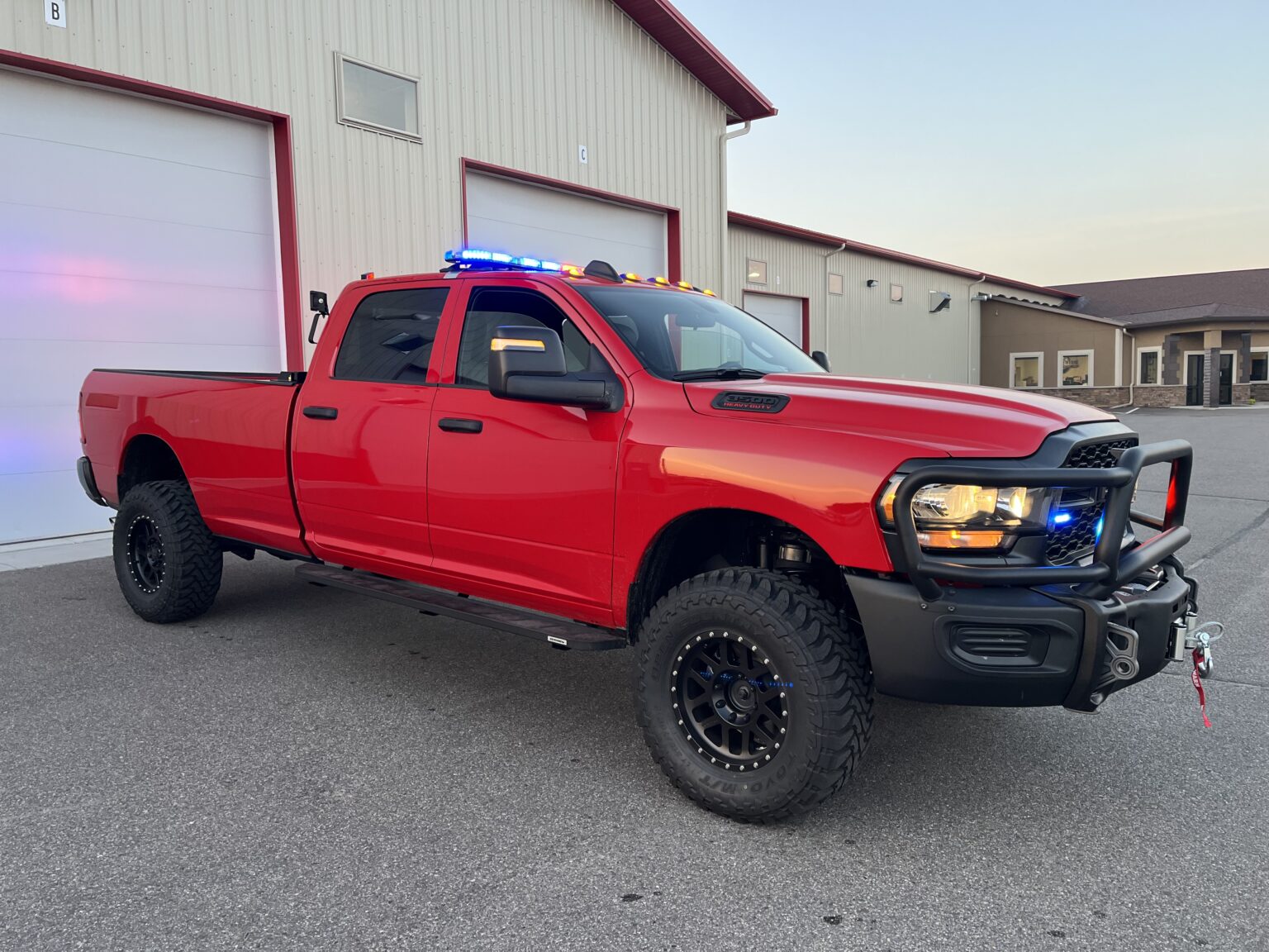 Red heavy-duty pickup truck with emergency lights and winch parked outside a garage.