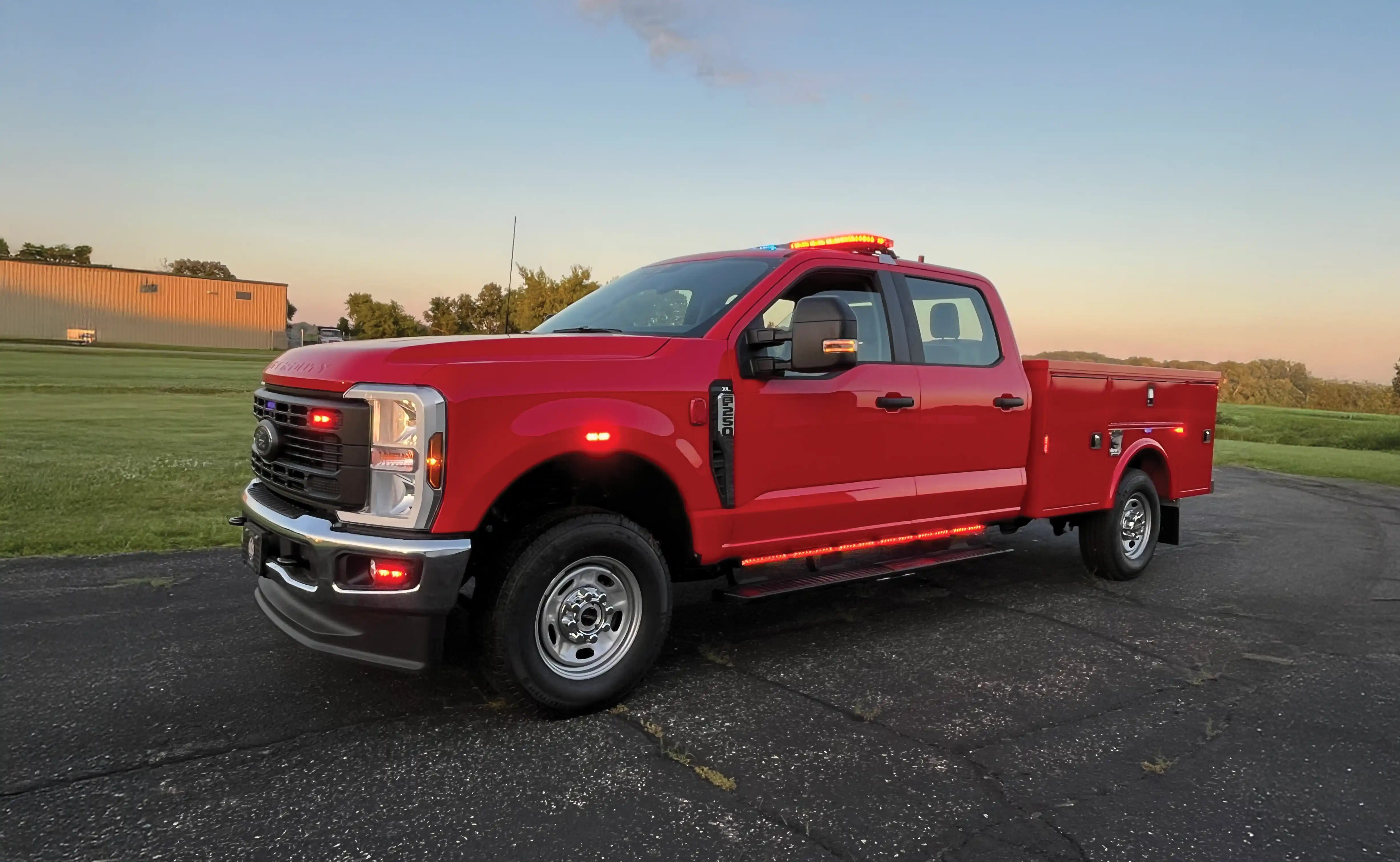 Red Ford F-250 pickup truck with flashing emergency lights parked on paved surface at dusk.