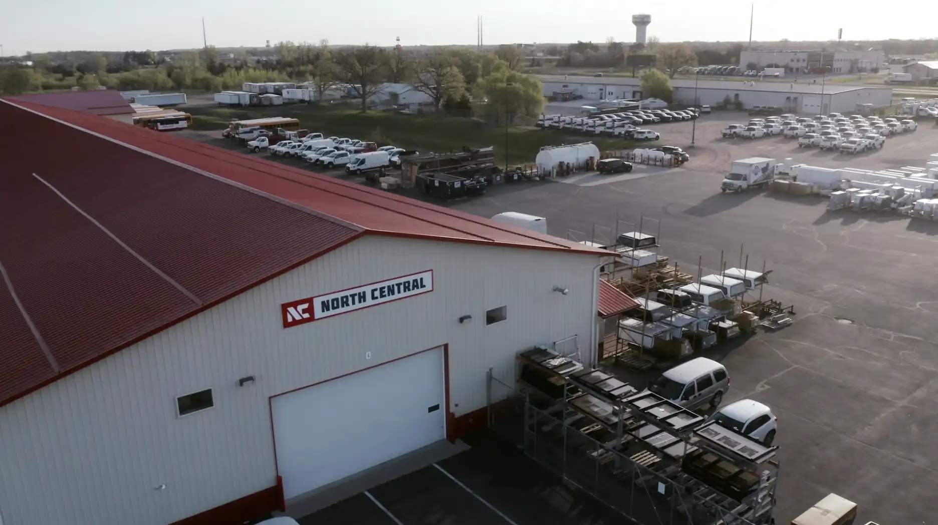 An industrial building with a red roof labeled North Central and a large parking lot filled with white vehicles.