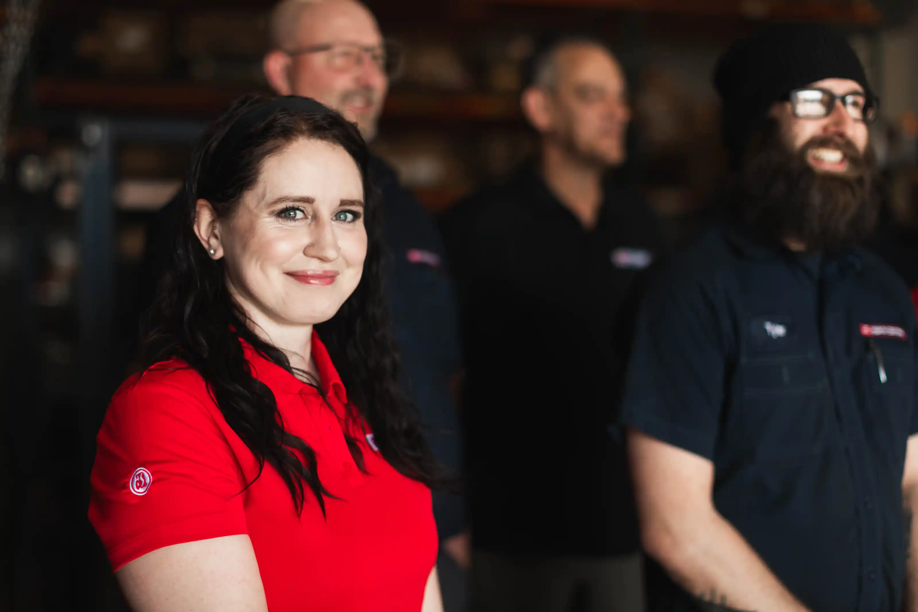 Smiling woman in red shirt with three men blurred in the background.