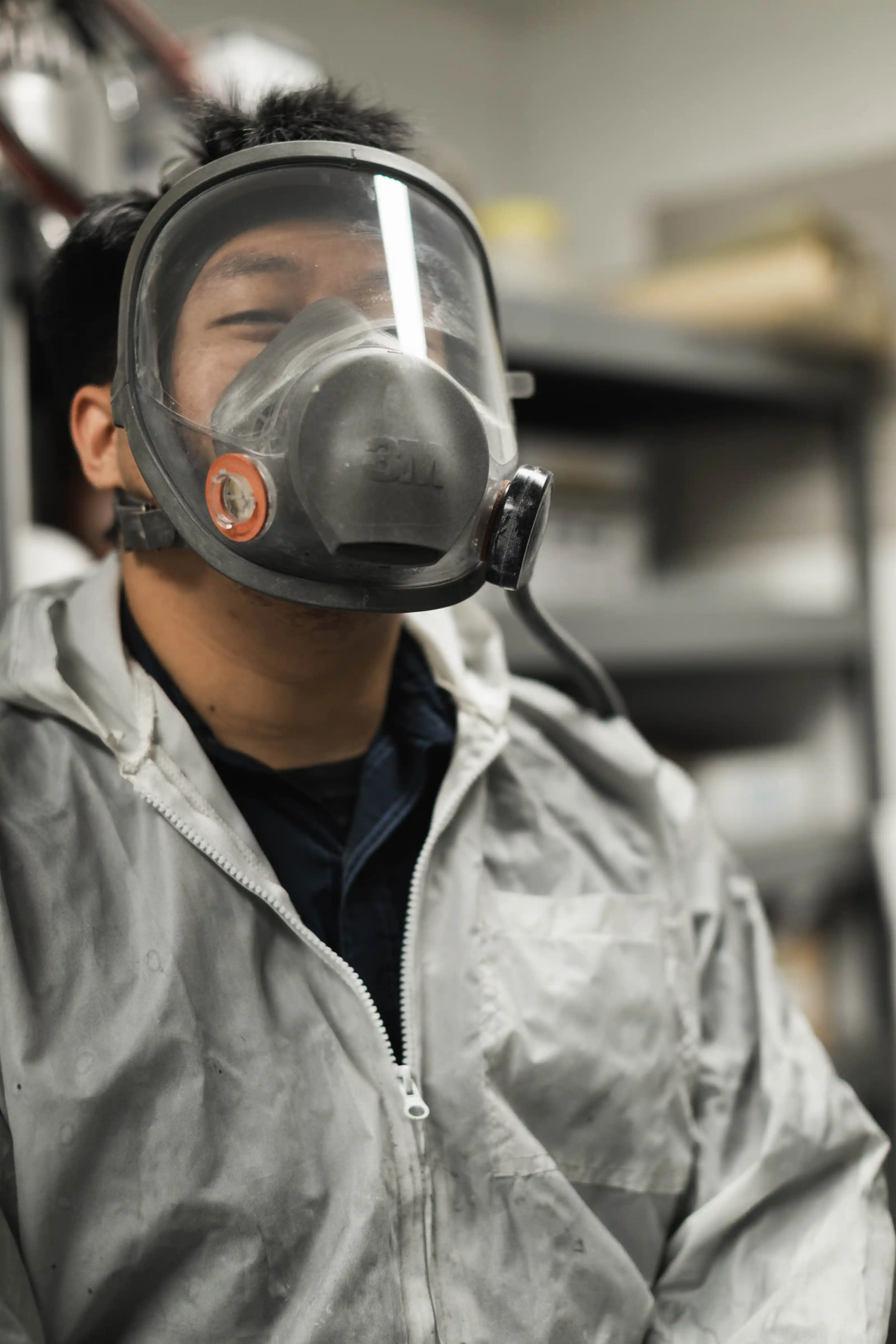 Person wearing a protective respirator mask and light-colored zippered jacket indoors.