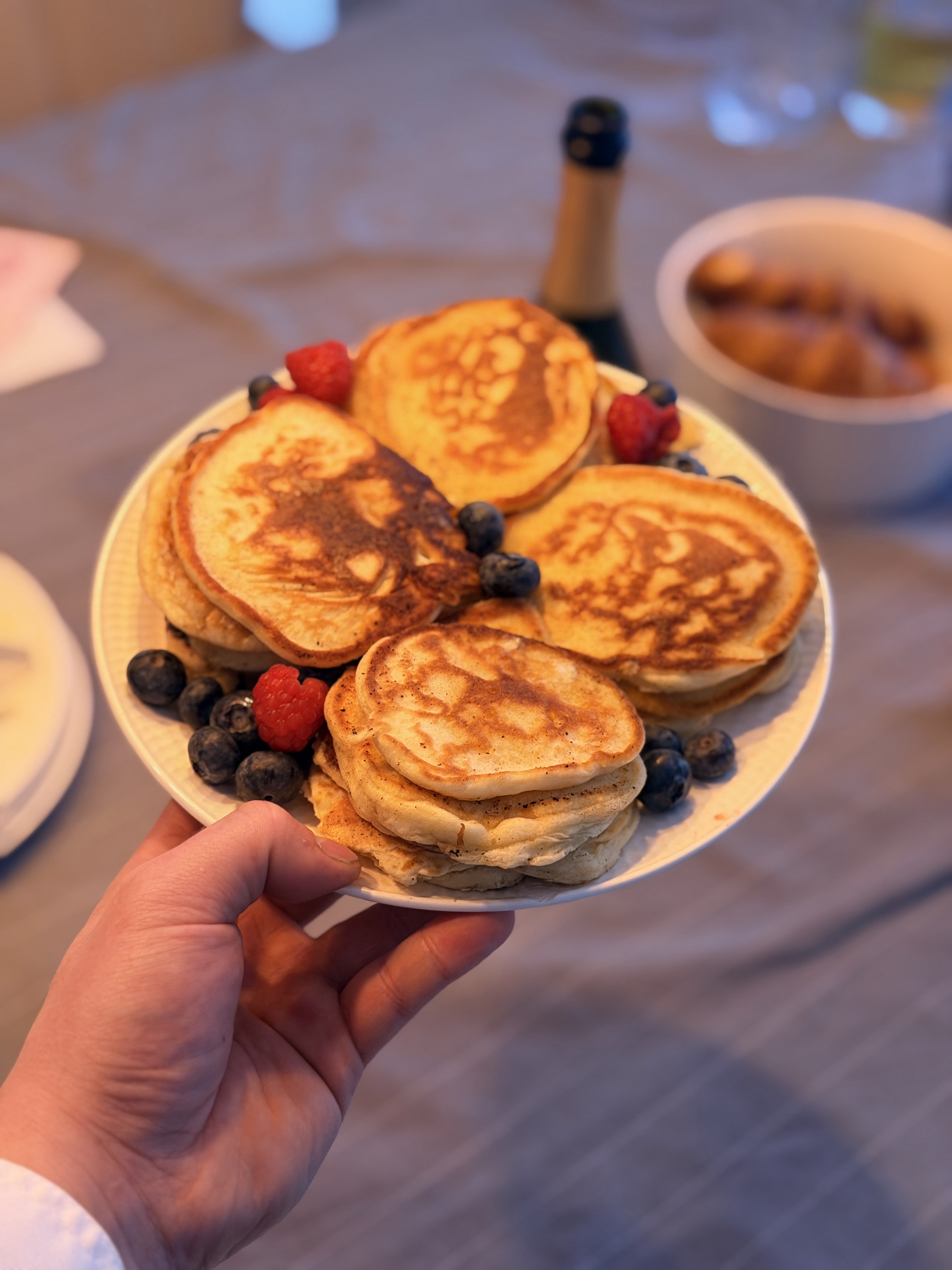 Hand houdt een bord met warme, goudbruine pannenkoeken omringd door blauwe bessen en frambozen.