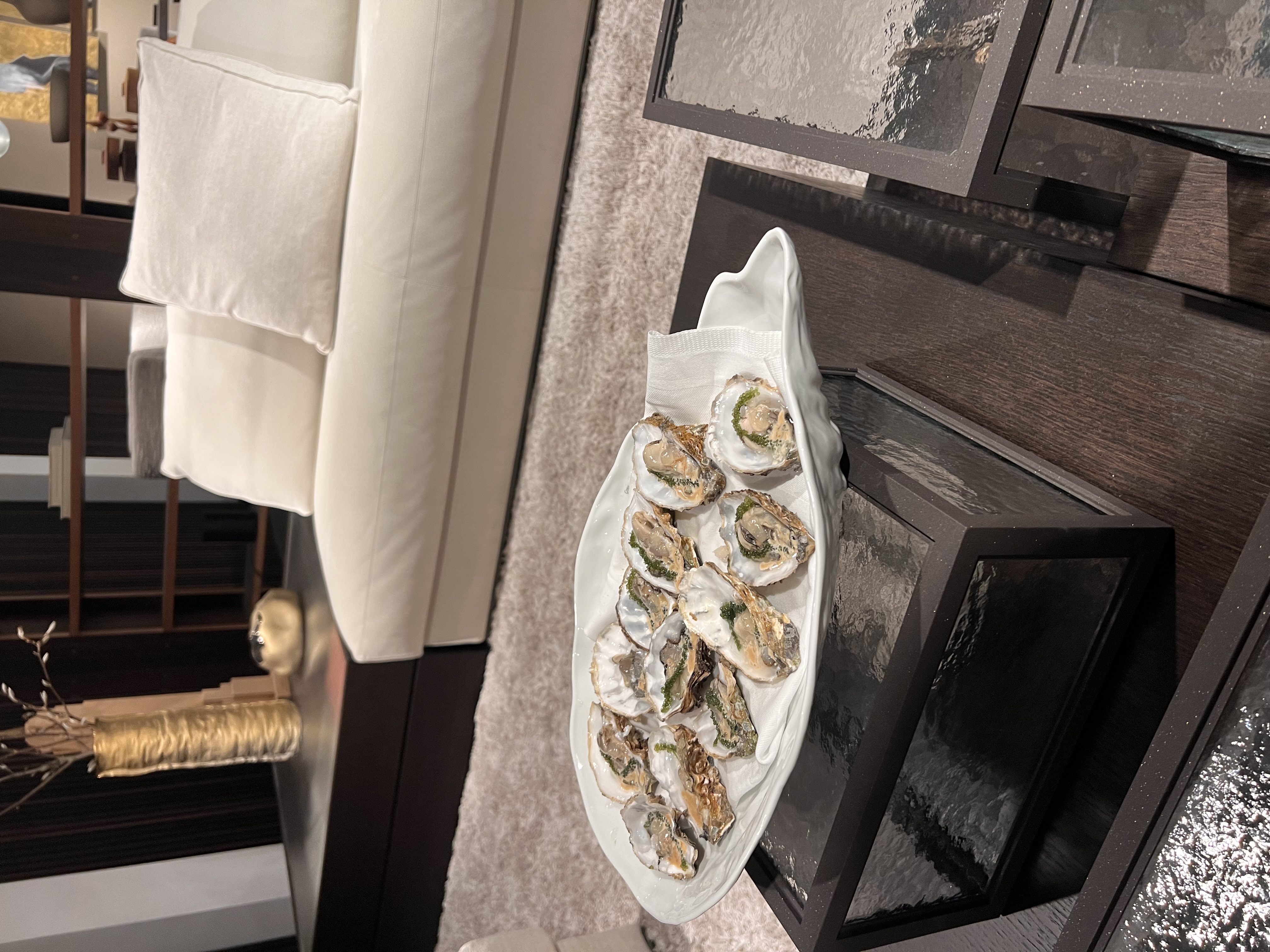 Schaal met verse oesters op een houten salontafel in een moderne woonkamer met een beige bank en een gouden vaas.