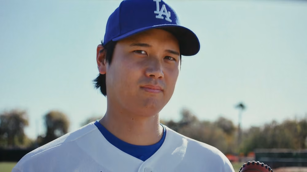 Man wearing Los Angeles Dodgers baseball cap and white jersey outdoors during daytime.