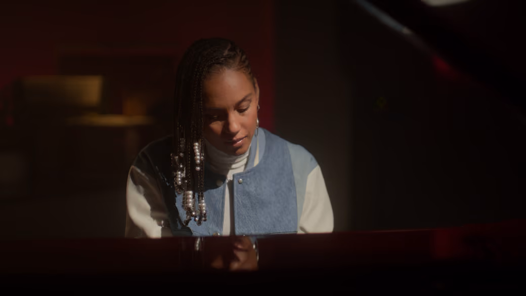 Woman with braided hair and pearls playing piano in dimly lit room.