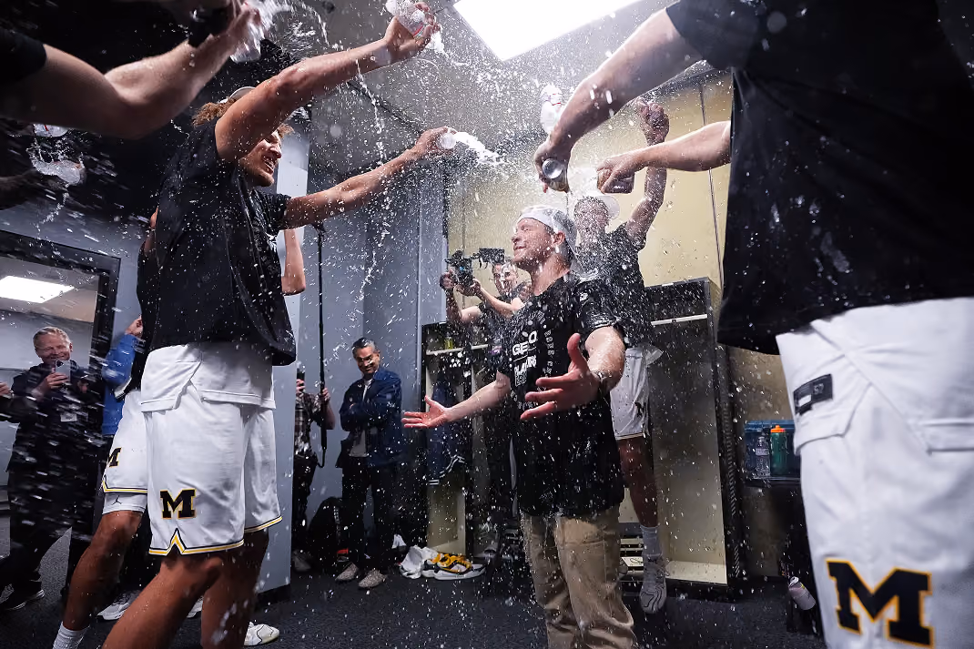 Basketball players celebrating in a locker room, spraying their coach with water.