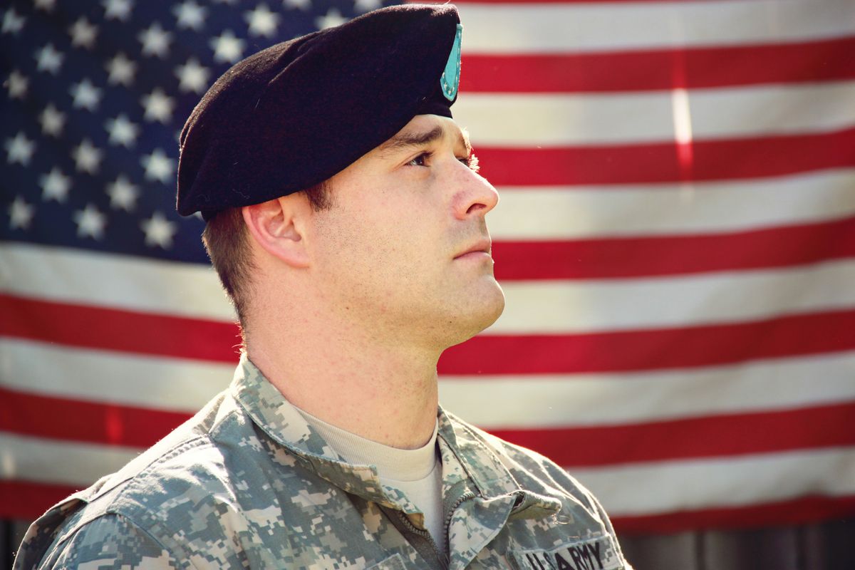 A service member in uniform in front of an American flag