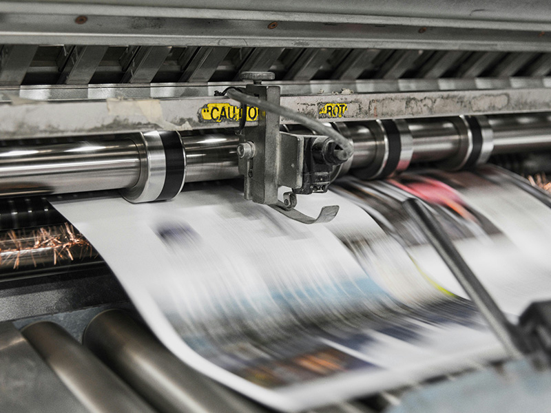 Newspapers quickly printed and moving through a printing press machine.