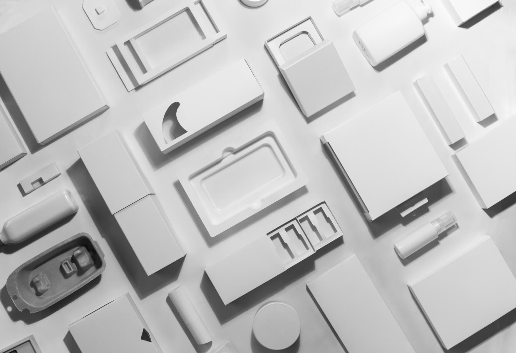 Various white blank product packaging designs including boxes, bottles, and trays arranged on a surface.