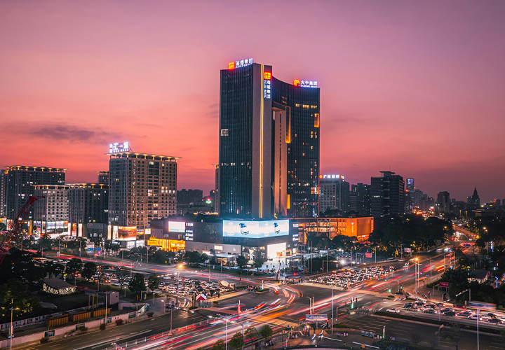 City traffic at a busy intersection with tall lit buildings under a purple sunset sky.