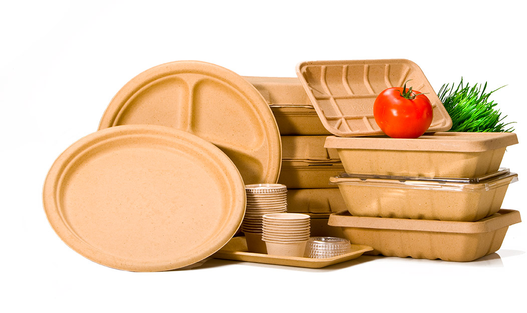 Stack of beige compostable food trays, plates, and cups with a tomato and green plant on top.