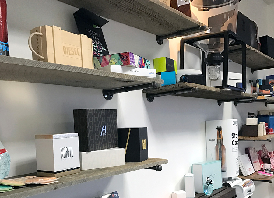 Wooden shelves mounted on wall displaying various cosmetic and perfume boxes and bottles in a store.