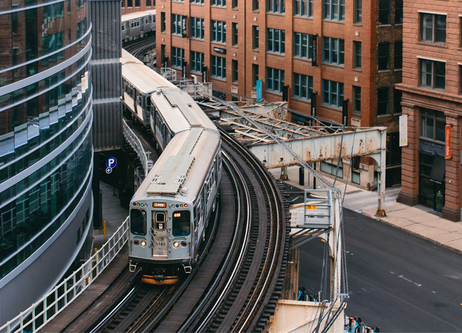 Silver elevated train curving through urban cityscape with brick and glass buildings.