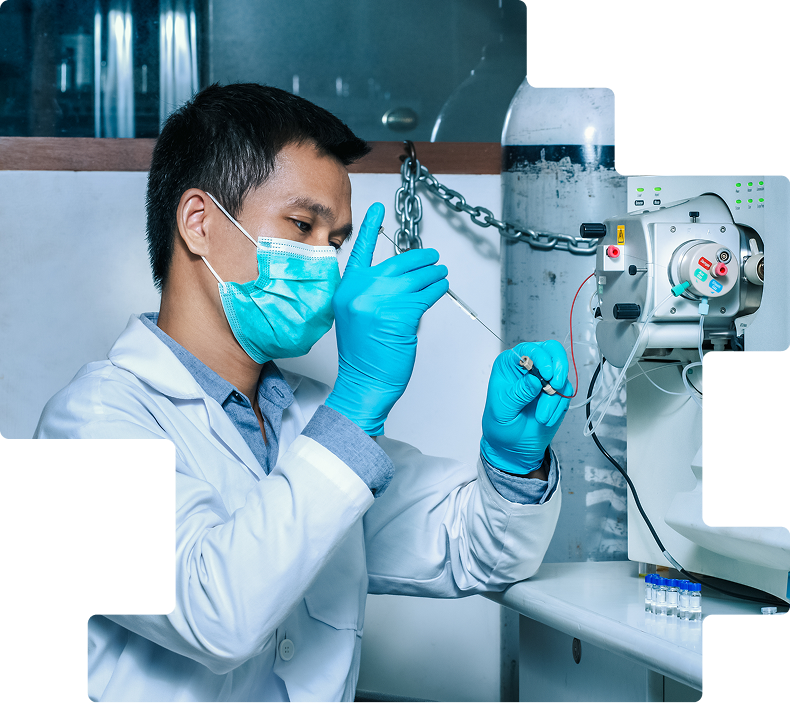 Masked lab worker in blue gloves connecting a sample line to analytical instrumentation