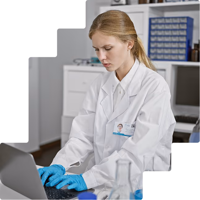 Female scientist in a lab coat and blue gloves entering data on a laptop in a laboratory