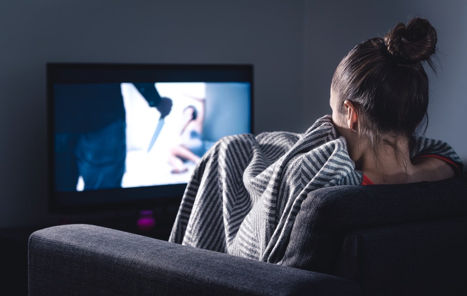 Woman curled up under gray blanket on couch while crime movie plays on TV screen | 7 Movies Like The Departed