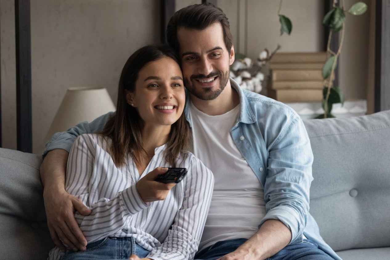 Pareja más joven sonriendo mientras ve una película | Películas para sentirse bien