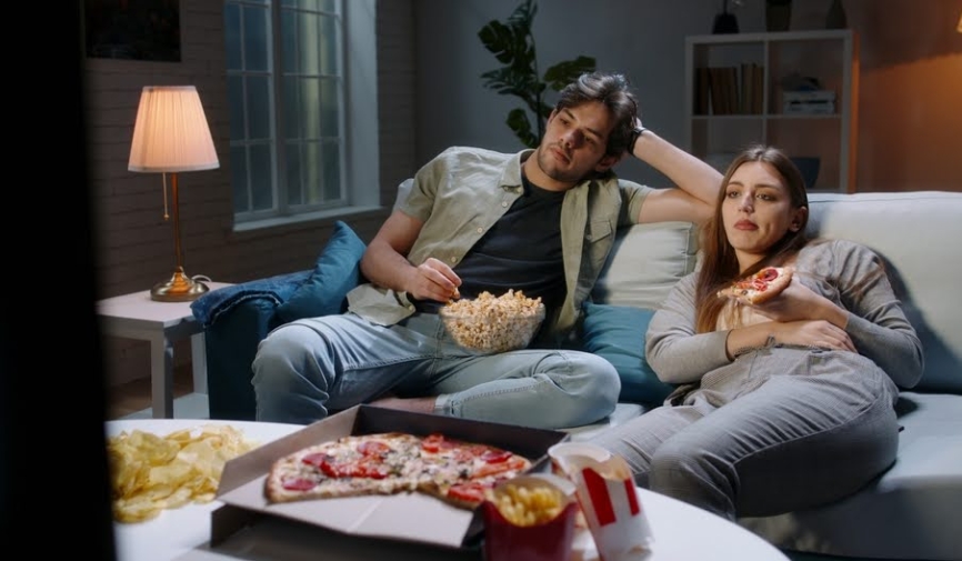 A young couple sitting on the couch while eating snacks | Best stoner movies