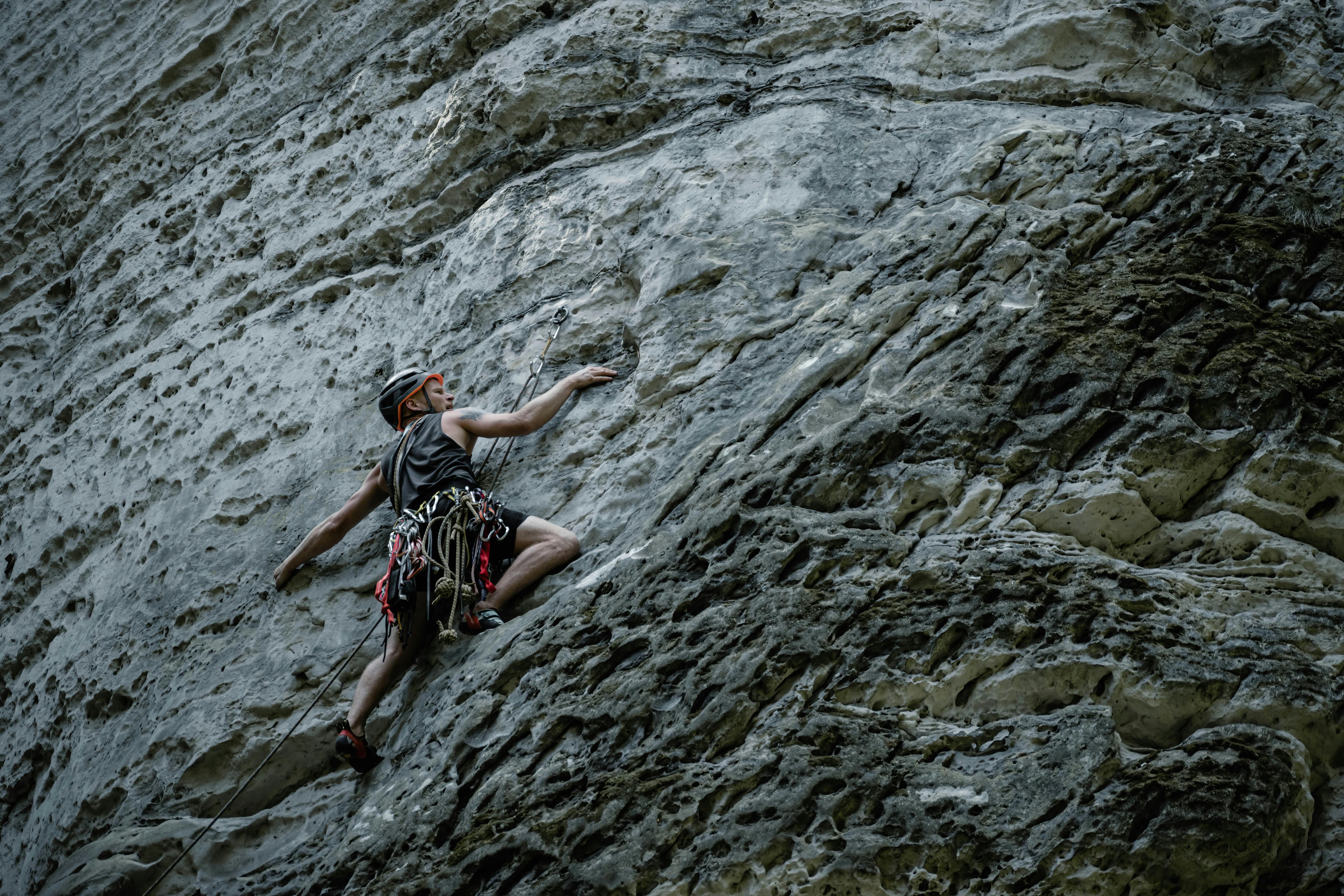 Man wearing helmet and climbing gear scaling a steep textured rock face during outdoor rock climbing.